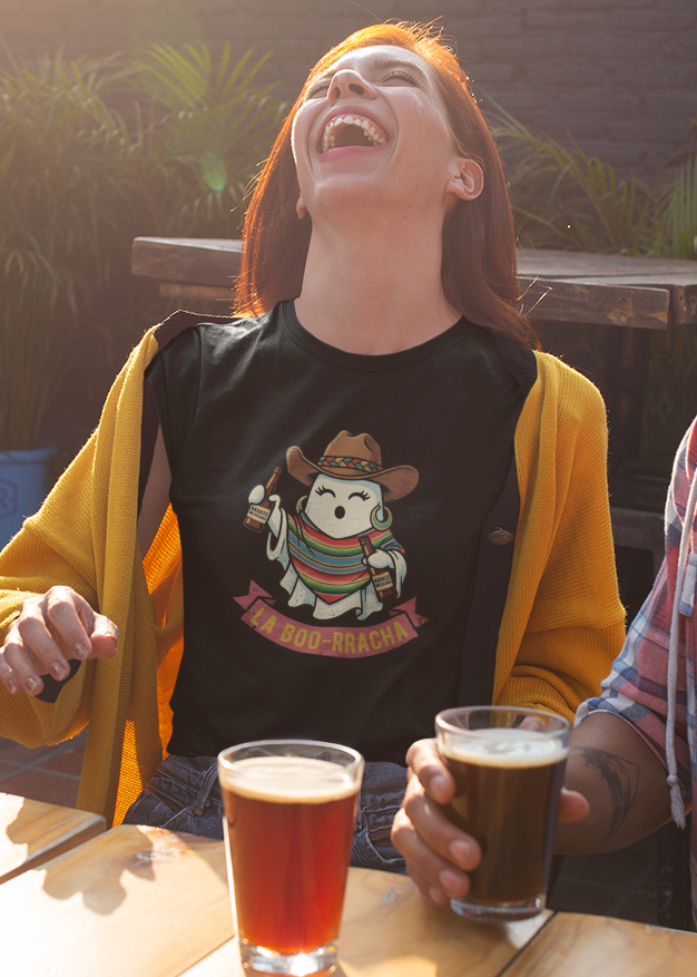 Black fitted women's t-shirt featuring an illustration of a cute ghost wearing a cowboy hat and colorful sarape holding drinks above text reading "LA BOO-RRACHA".