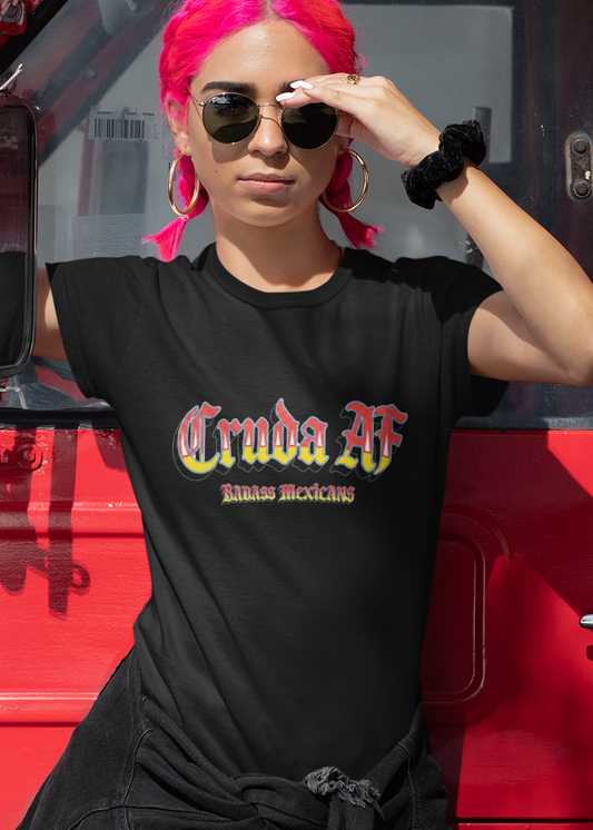 A black fitted women's crew-neck t-shirt featuring the text "Cruda AF" printed across the chest in a bold, stylized Gothic font. The letters feature a horizontal color gradient transition from red at the top, fading into yellow and white at the bottom, outlined in black with a heavy black drop shadow. Directly below, the words "BADASS MEXICANS" are printed in a smaller, matching Gothic font with the same red, yellow, and white gradient and drop shadow effect.
