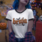 White ringer t-shirt with black collar and cuffs featuring the word "BRUJA" in bold orange font with a bat and broomstick graphic.