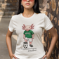 A white crew-neck t-shirt  featuring a colorful graphic illustration of a cute pink axolotl character dressed in a green Mexico soccer jersey, white shorts, and soccer cleats. The axolotl is standing with one foot on a classic black and white soccer ball. Below the design, it reads "El Axolotl by BADASS MEXICANS" with a cursive signature.