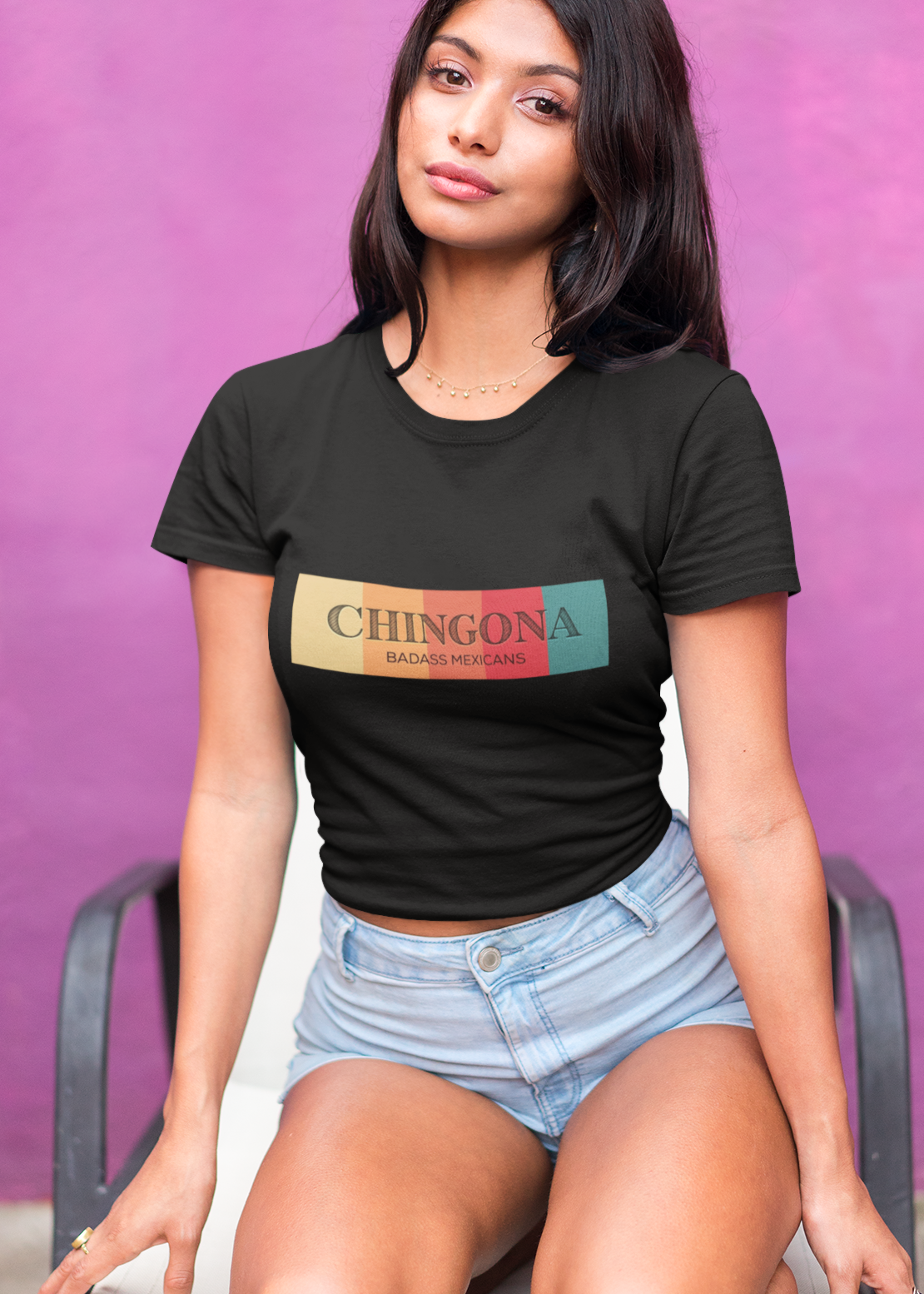 A black fitted women's crew-neck t-shirt featuring a horizontal graphic design across the chest. The design features five vertical, vintage-toned color blocks lined up side-by-side in pastel yellow, soft orange, terracota red, deep pink, and muted teal. Overlaid across these colorful blocks, the word "CHINGONA" is printed in a large, elegant dark gray serif font, with the words "BADASS MEXICANS" written directly underneath in a smaller, clean sans-serif typeface.