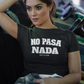 Woman wearing a black unisex t-shirt with the phrase “No Pasa Nada” printed in bold white letters, seated in an arcade environment with colorful lights in the background.
