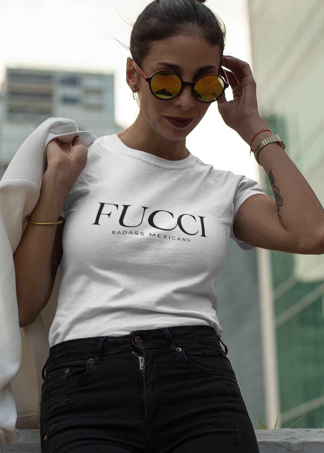 A white lifestyle t-shirt featuring the word "FUCCI" printed in a large, elegant black serif font across the chest. Below it, the brand name "BADASS MEXICANS" is printed in a smaller, clean sans-serif font.