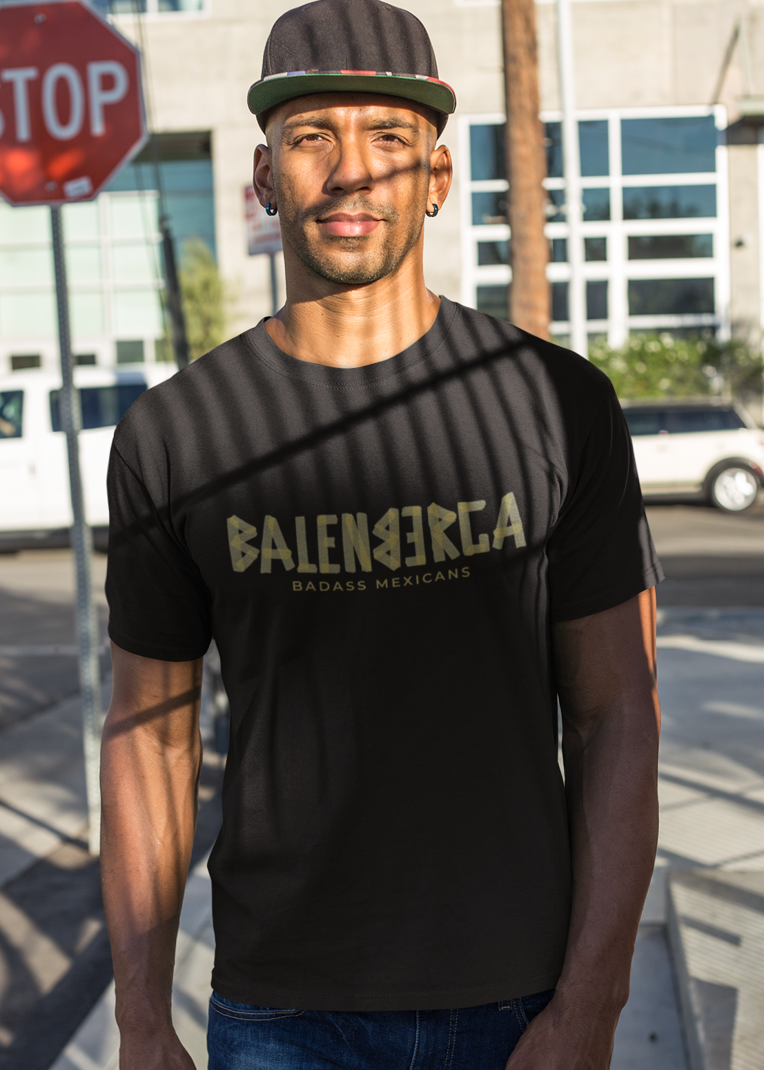 A black streetwear t-shirt showcasing the word "BALENBERGA" across the chest in a heavy, textured, geometric block font with alternating mirrored letters in an olive-beige tone. Underneath, "BADASS MEXICANS" is printed in a clean, sharp matching font.