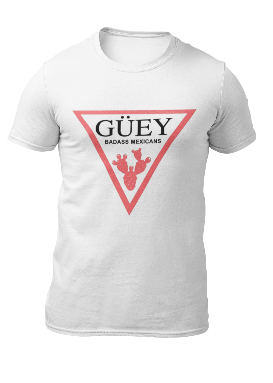 A white crew-neck t-shirt featuring a large, inverted pinkish-red triangle graphic printed on the chest. Inside the upper section of the triangle, the word "GÜEY" is written in a bold, black serif font, with the words "BADASS MEXICANS" printed right underneath in a smaller black sans-serif font. Centered at the bottom point of the triangle is a detailed graphic illustration of a prickly pear cactus (nopal) in a matching pinkish-red color.