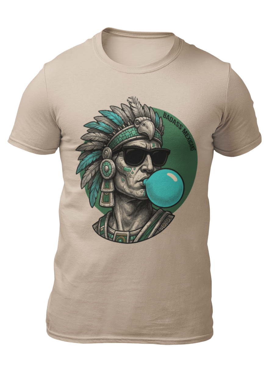 A sand crew-neck t-shirt featuring a circular graphic illustration on the chest. The design depicts an Aztec ruler or warrior chief in profile, wearing a highly detailed traditional feathered headdress and ear spools in shades of turquoise, green, and gray. The character is styled with a modern twist, wearing black sunglasses and blowing a large, bright light-blue bubblegum bubble. The entire illustration is set against a dark green solid circular background with the words "BADASS MEXICANS" written