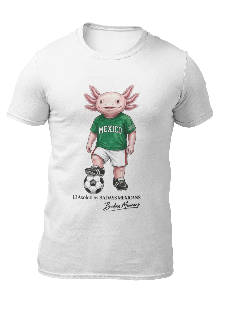 A white crew-neck t-shirt  featuring a colorful graphic illustration of a cute pink axolotl character dressed in a green Mexico soccer jersey, white shorts, and soccer cleats. The axolotl is standing with one foot on a classic black and white soccer ball. Below the design, it reads "El Axolotl by BADASS MEXICANS" with a cursive signature.
