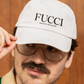 showing a close-up, front-facing view of a classic white dad hat. The word "FUCCI" is prominently embroidered across the front panel in a large, elegant black serif font, with the words "BADASS MEXICANS" stitched right below it in a smaller, clean sans-serif typeface.