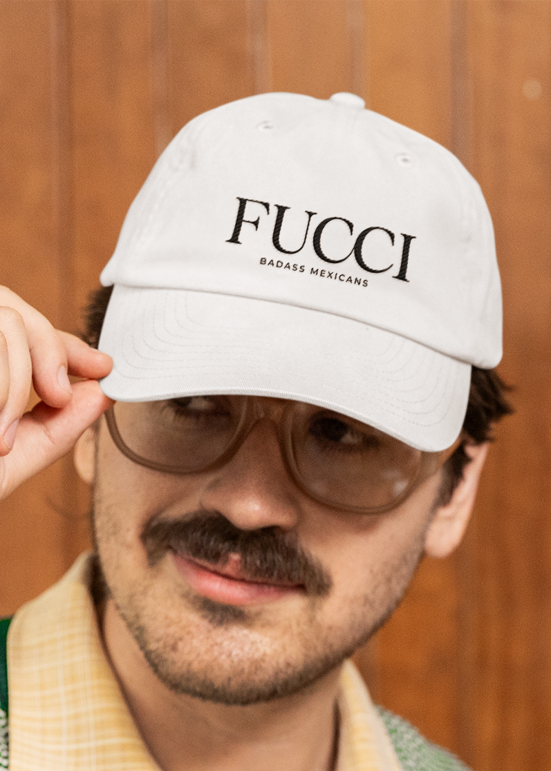 showing a close-up, front-facing view of a classic white dad hat. The word "FUCCI" is prominently embroidered across the front panel in a large, elegant black serif font, with the words "BADASS MEXICANS" stitched right below it in a smaller, clean sans-serif typeface.
