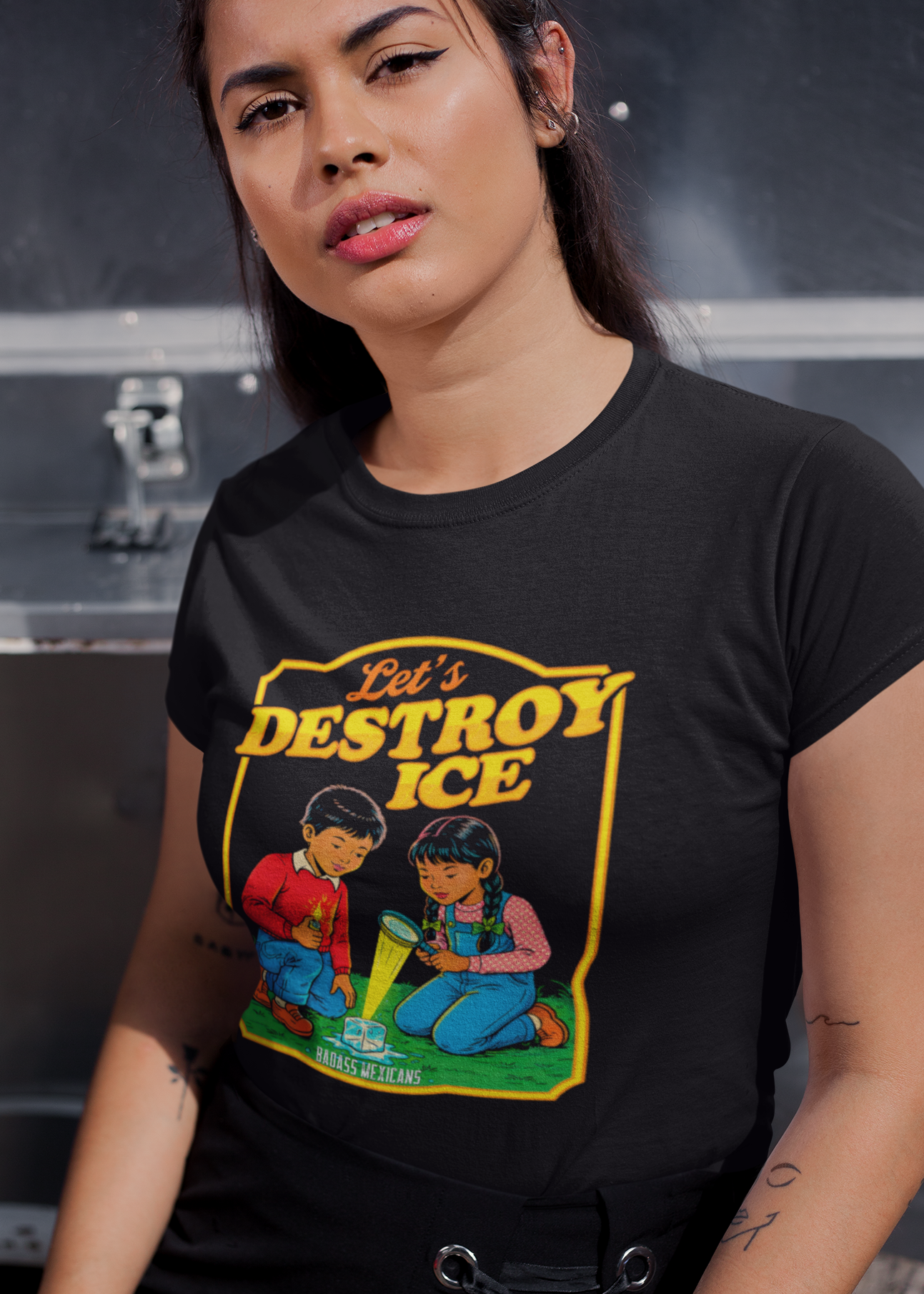A woman wearing a black t-shirt with a vintage-style illustration of a boy and a girl melting an ice cube and the phrase “Let’s Destroy ICE” in bold retro typography.
