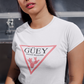 A white crew-neck t-shirt featuring a large, inverted pinkish-red triangle graphic printed on the chest. Inside the upper section of the triangle, the word "GÜEY" is written in a bold, black serif font, with the words "BADASS MEXICANS" printed right underneath in a smaller black sans-serif font. Centered at the bottom point of the triangle is a detailed graphic illustration of a prickly pear cactus (nopal) in a matching pinkish-red color.