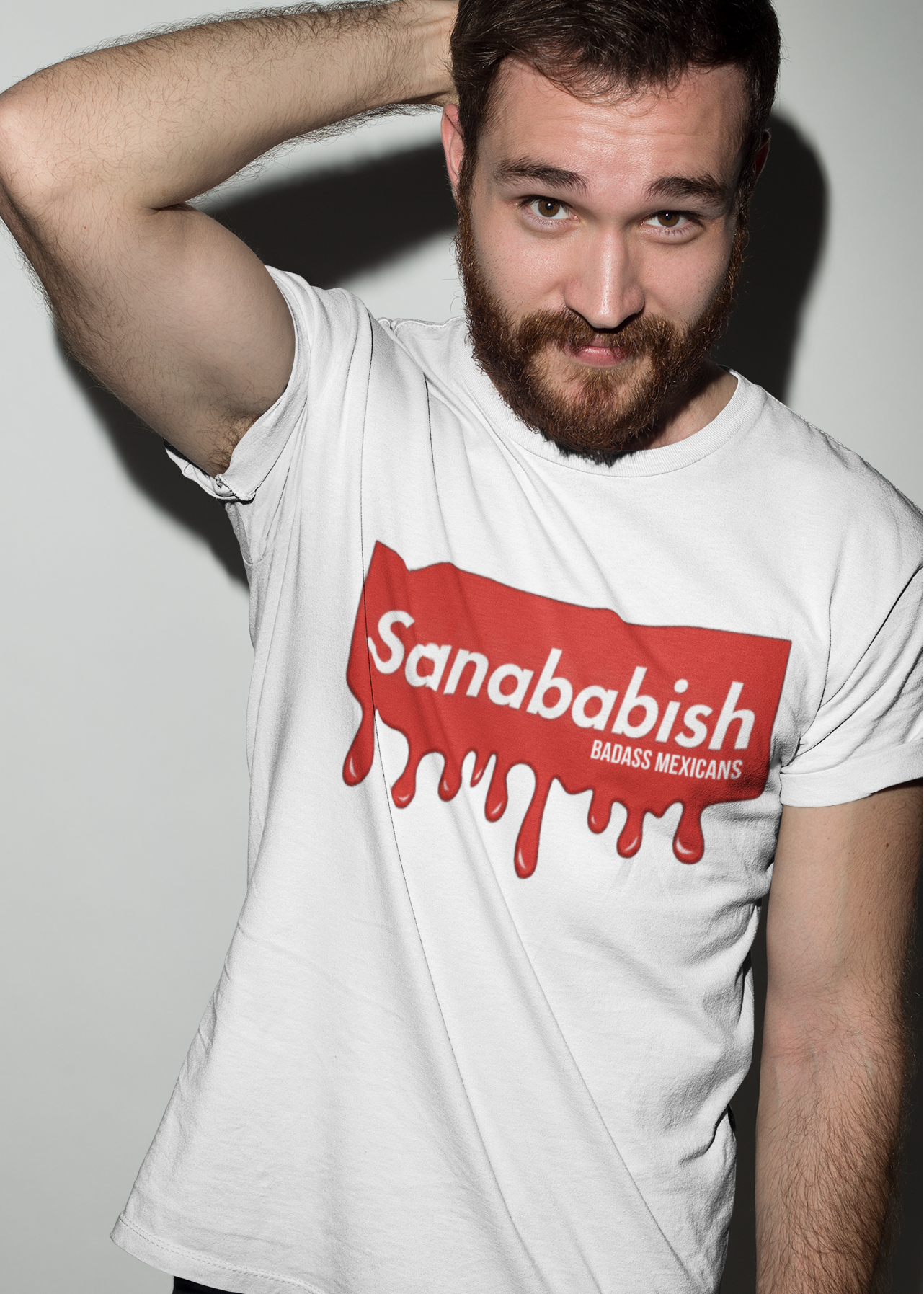A white crew-neck t-shirt featuring a solid red rectangular box graphic on the chest. Inside the box, the word "Sanababish" is printed in a bold white, slanted font, with the words "BADASS MEXICANS" in smaller white letters beneath it. The bottom edge of the red box is styled to look like wet paint, with thick red droplets dripping down onto the fabric.