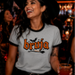 Grey ringer t-shirt with black collar and cuffs featuring the word "BRUJA" in bold orange font with a bat and broomstick graphic.