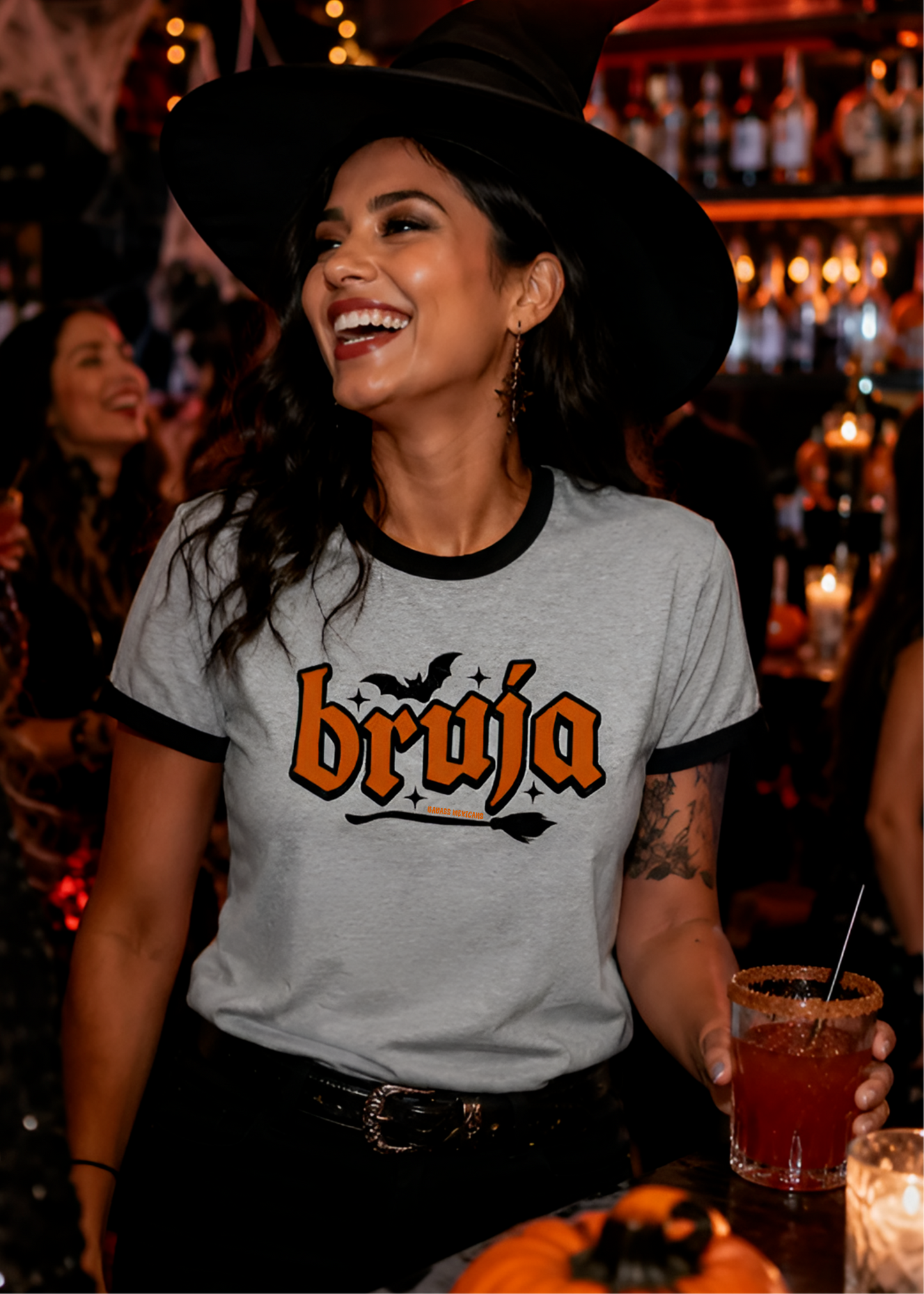 Grey ringer t-shirt with black collar and cuffs featuring the word "BRUJA" in bold orange font with a bat and broomstick graphic.