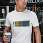 An white crew-neck t-shirt featuring a graphic design printed across the chest. The design consists of five vertical color blocks lined up side-by-side in white, beige, gold, blue, and dark gray. Overlaid on these blocks, the word "CHINGON" is printed in a large, elegant dark gray serif font, with the words "BADASS MEXICANS" written directly underneath in a smaller, clean sans-serif typeface.
