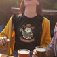 Black fitted women's t-shirt featuring an illustration of a cute ghost wearing a cowboy hat and colorful sarape holding drinks above text reading "LA BOO-RRACHA".