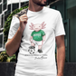 A white crew-neck t-shirt  featuring a colorful graphic illustration of a cute pink axolotl character dressed in a green Mexico soccer jersey, white shorts, and soccer cleats. The axolotl is standing with one foot on a classic black and white soccer ball. Below the design, it reads "El Axolotl by BADASS MEXICANS" with a cursive signature.