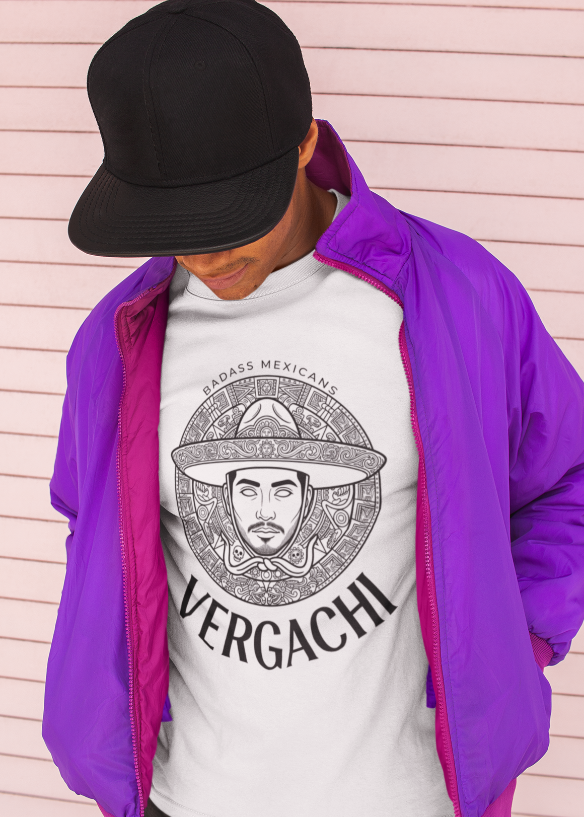 A white t-shirt featuring a large black graphic. The design includes a circular Aztec calendar-style background with a stylized man wearing a traditional Mexican charro hat in the center. The word "VERGACHI" is printed in a bold, arched serif font underneath the graphic, with "BADASS MEXICANS" in a small arch above it.