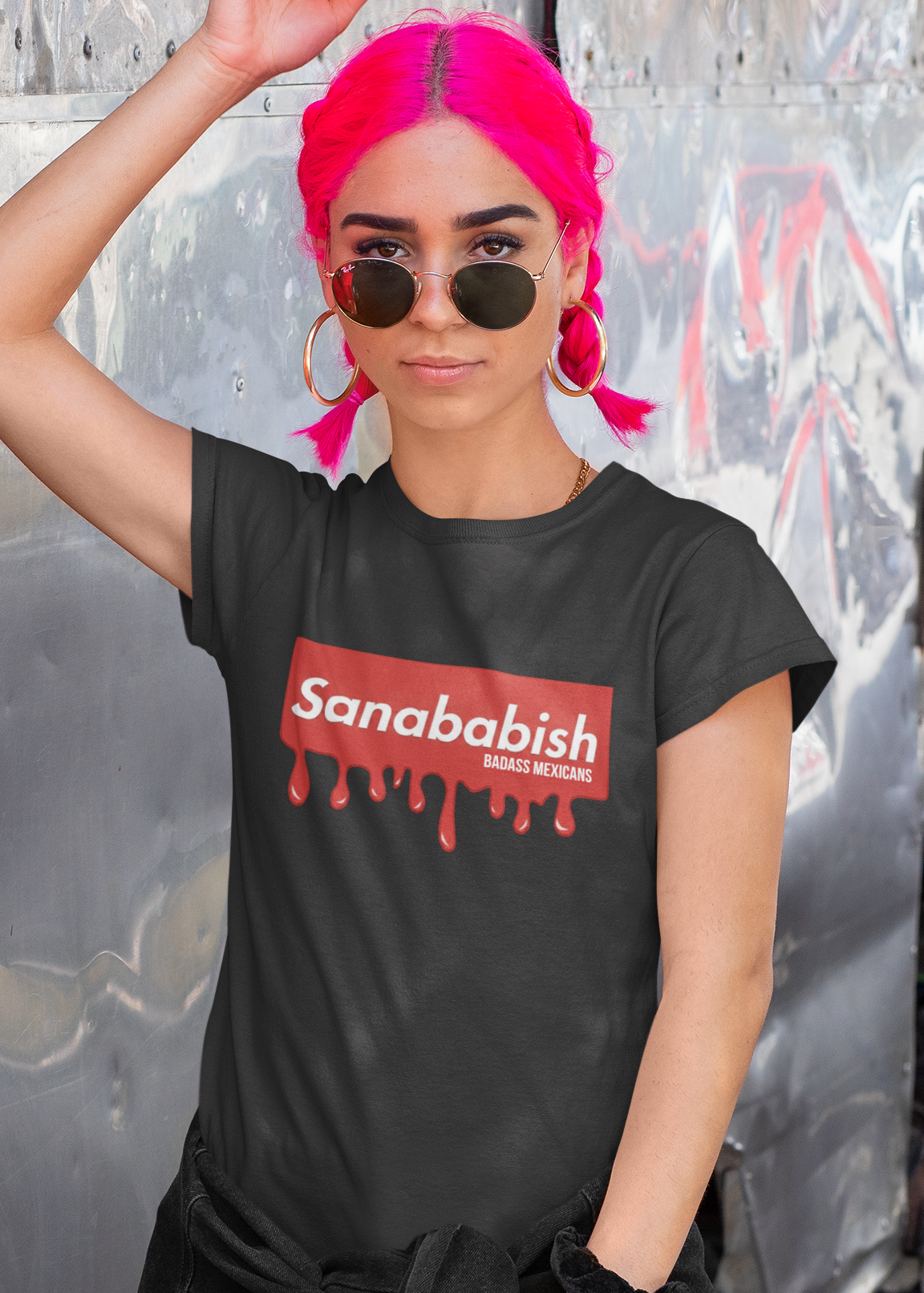 A black crew-neck t-shirt featuring a solid red rectangular box graphic on the chest. Inside the box, the word "Sanababish" is printed in a bold white, slanted font, with the words "BADASS MEXICANS" in smaller white letters beneath it. The bottom edge of the red box is styled to look like wet paint, with thick red droplets dripping down onto the fabric.