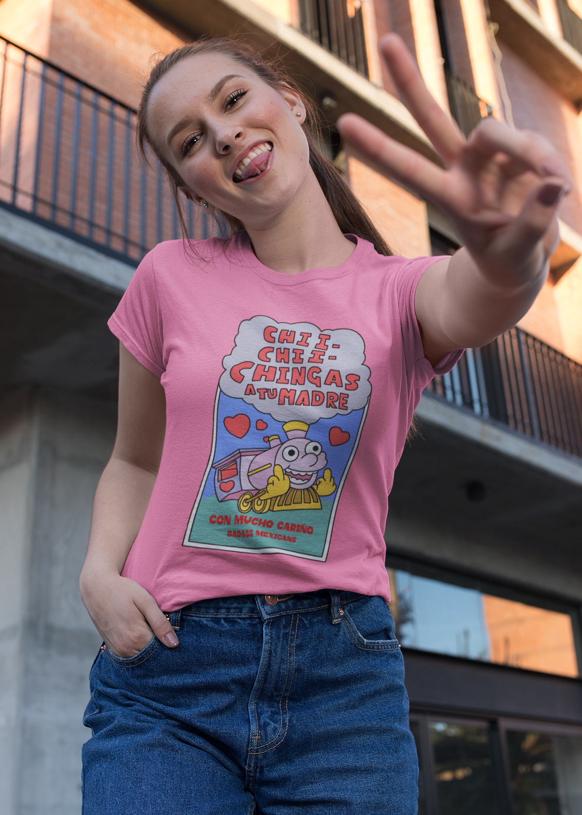 Woman wearing pink t-shirt featuring a colorful Valentine-style illustration with Spanish text that reads "Chingas a tu Madre" “Con Cariño,” designed as a humorous and playful Mexican-inspired message.