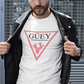 A white crew-neck t-shirt featuring a large, inverted pinkish-red triangle graphic printed on the chest. Inside the upper section of the triangle, the word "GÜEY" is written in a bold, black serif font, with the words "BADASS MEXICANS" printed right underneath in a smaller black sans-serif font. Centered at the bottom point of the triangle is a detailed graphic illustration of a prickly pear cactus (nopal) in a matching pinkish-red color.
