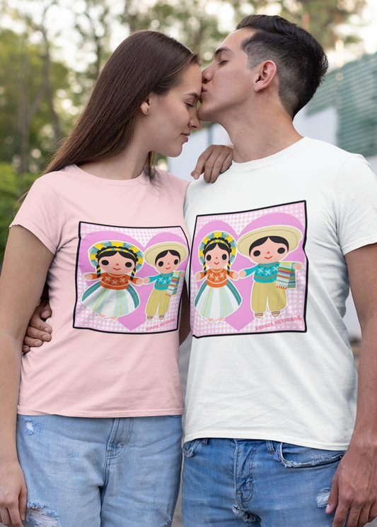 A man kissing his girlfriend on the street wearing matching Valentine’s Day t-shirts featuring colorful Mexican folk art dolls inside heart-shaped designs, symbolizing love, culture, and togetherness.