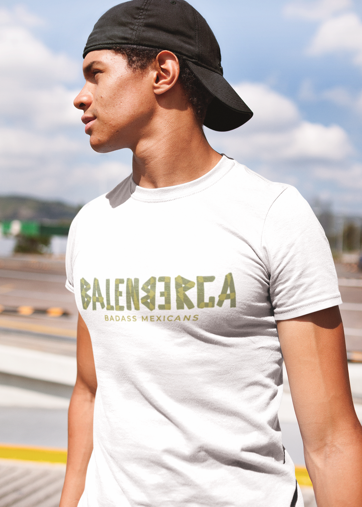 A white streetwear t-shirt showcasing the word "BALENBERGA" across the chest in a heavy, textured, geometric block font with alternating mirrored letters in an olive-beige tone. Underneath, "BADASS MEXICANS" is printed in a clean, sharp matching font.