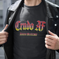 A black crew-neck t-shirt featuring the text "Crudo AF" printed across the chest in a bold, stylized Gothic font. The letters have a horizontal color gradient transition from red at the top, fading into yellow and white at the bottom, outlined in black with a heavy black drop shadow. Directly below, the words "BADASS MEXICANS" are printed in a smaller, matching Gothic font with the same red, yellow, and white gradient and drop shadow effect.