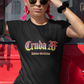 A black fitted women's crew-neck t-shirt featuring the text "Cruda AF" printed across the chest in a bold, stylized Gothic font. The letters feature a horizontal color gradient transition from red at the top, fading into yellow and white at the bottom, outlined in black with a heavy black drop shadow. Directly below, the words "BADASS MEXICANS" are printed in a smaller, matching Gothic font with the same red, yellow, and white gradient and drop shadow effect.