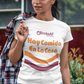 A woman wearing a white t-shirt featuring the phrase “Hay Comida En La Casa” in a retro instant noodle-inspired design with orange and brown accents.