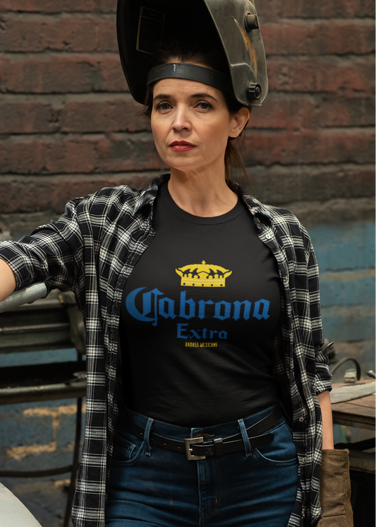 A woman wearing a black t-shirt featuring the phrase “Cabrona Extra” in bold blue lettering with a gold crown above, inspired by a classic beer-style typography.
