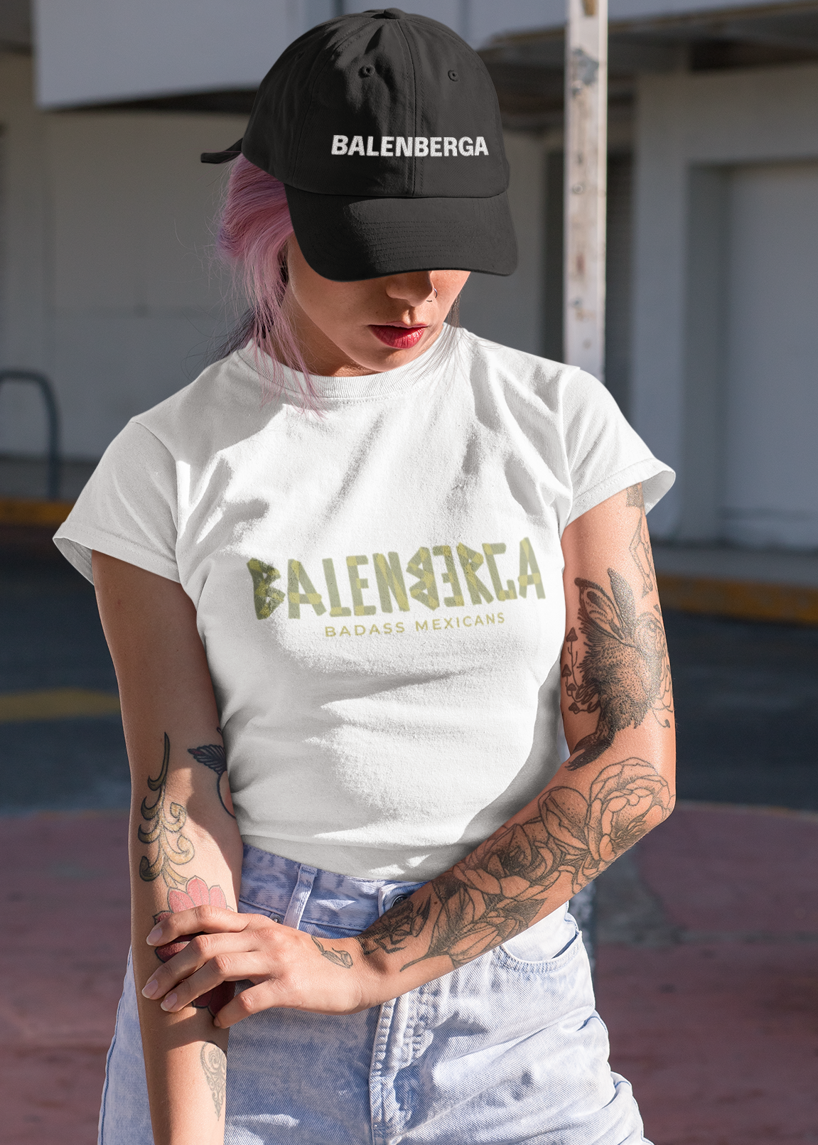 A white streetwear t-shirt showcasing the word "BALENBERGA" across the chest in a heavy, textured, geometric block font with alternating mirrored letters in an olive-beige tone. Underneath, "BADASS MEXICANS" is printed in a clean, sharp matching font.