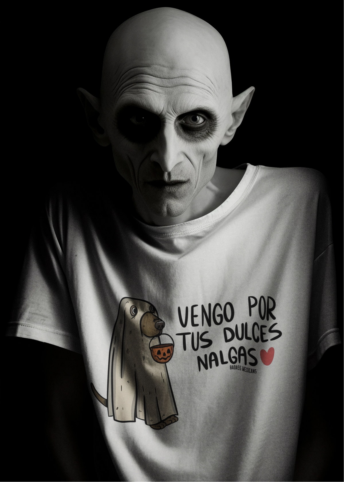 White t-shirt featuring an illustration of a dog dressed as a sheet ghost holding a pumpkin bucket next to text reading "VENGO POR TUS DULCES NALGAS".