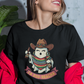 Black fitted women's t-shirt featuring an illustration of a cute ghost wearing a cowboy hat and colorful sarape holding drinks above text reading "LA BOO-RRACHA".